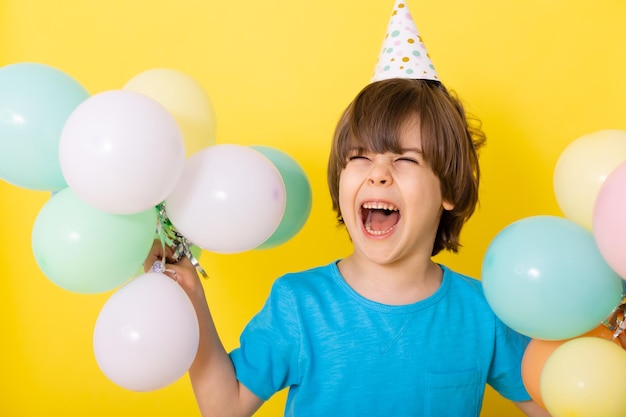 Bel ragazzino di compleanno in camicia blu e cappello con palloncini sfondo giallo buon compleanno