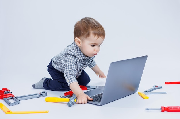 A handsome little boy 23 years old in a shirt on a white background is looking at a laptop A child is playing with a portable laptop