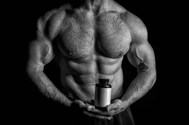 Handsome macho man or sexy muscular guy with athlete body and torso holds plastic jar or container with nutrition or pills on black background