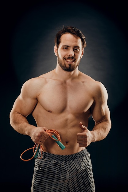 A handsome male bodybuilder with a rope in his hands on a dark background