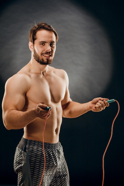 A handsome male bodybuilder with a rope in his hands on a dark background