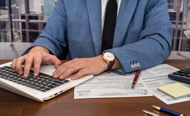 Handsome male businessman sitting at the table and filling out US tax forms 1040