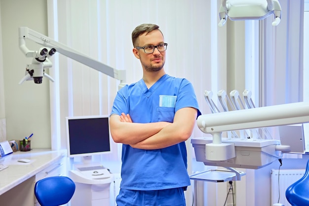 Handsome male dentist in a room with medical equipment on background.