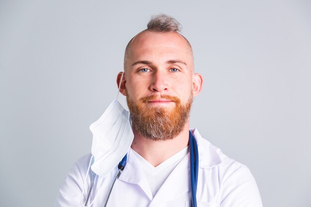 Photo handsome male doctor on gray wall with takes off  protective medical mask