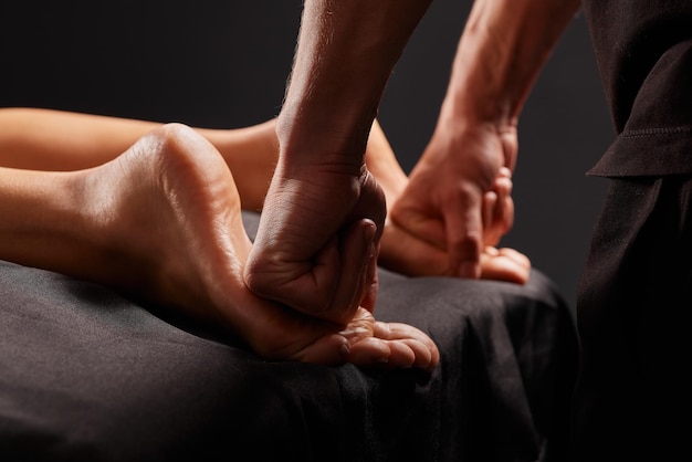 handsome male masseur doing a massage on a girl's leg on a black background concept of therapeutic relaxing massage