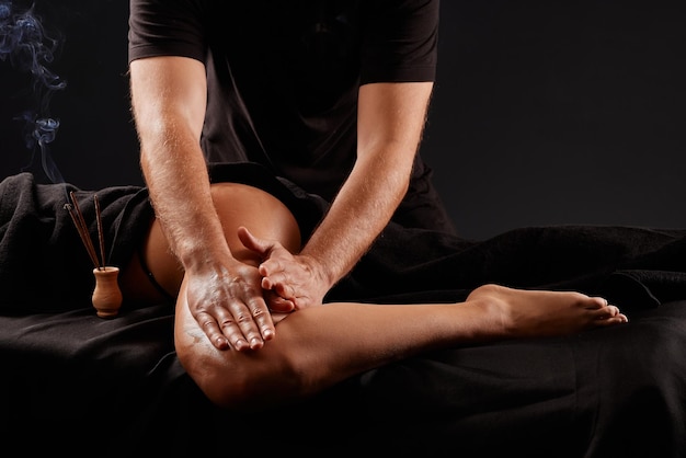 handsome male masseur doing a massage on a girls leg on a black background concept of therapeutic relaxing massage