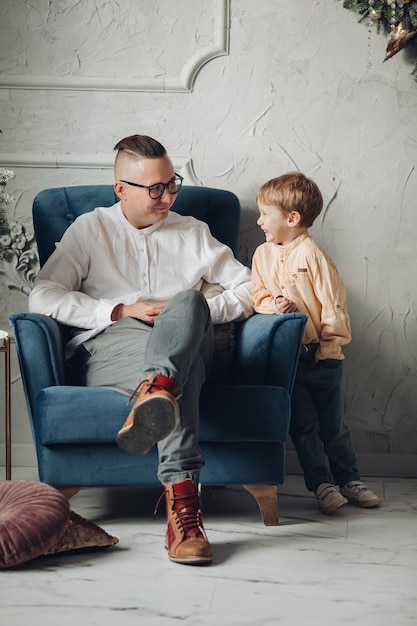 Handsome male person expressing positivity while sitting on armchair and listening to his son
