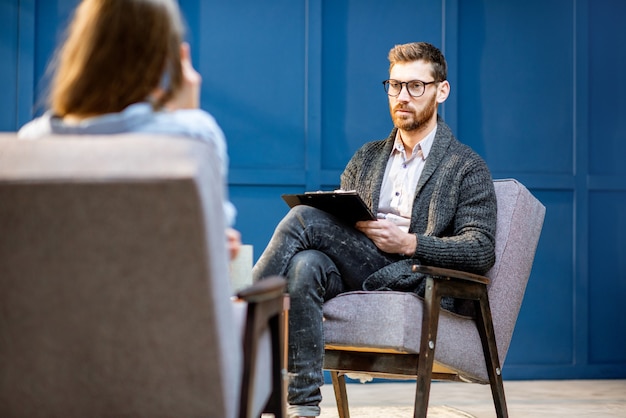 Handsome male psychologist listening to the woman client sitting during psychological session in the blue office interior