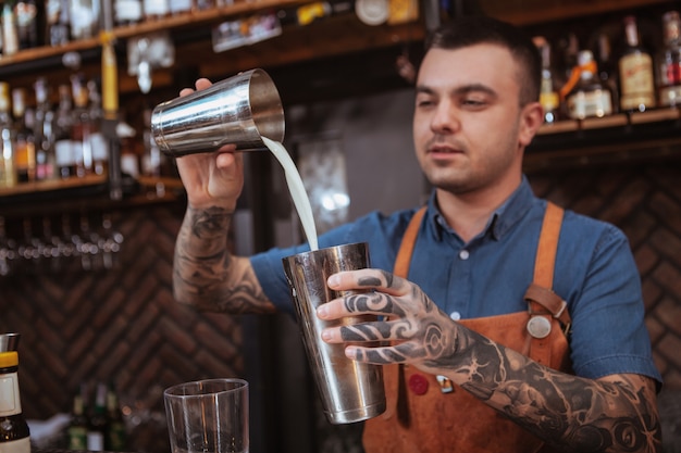 飲み物を準備するハンサムな男性の入れ墨のバーテンダー