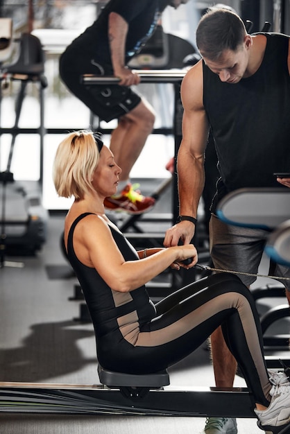 Handsome male trainer with athletic body helps girl client to\
perform proper exercises on the simulator the concept of training\
with a coach man