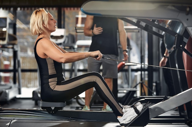 Handsome male trainer with athletic body helps girl client to\
perform proper exercises on the simulator the concept of training\
with a coach man