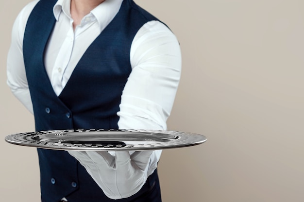 잘 생긴 남자 웨이터, 흰 셔츠, 은색 쟁반, 그의 뒤 손을 보유하고 있습니다. 레스토랑에서 고객을 제공하는 대기 직원의 개념.