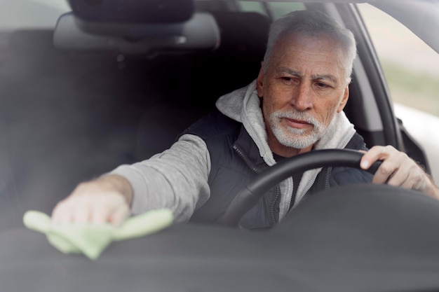 Handsome man 6070 years old cleaning and wiping the interior of his car Car maintenance concept