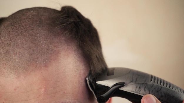 Handsome man in the bathroom shaves his head with an electric razor due to coronavirus quarantine selfisolation part of the head in the frame closeup