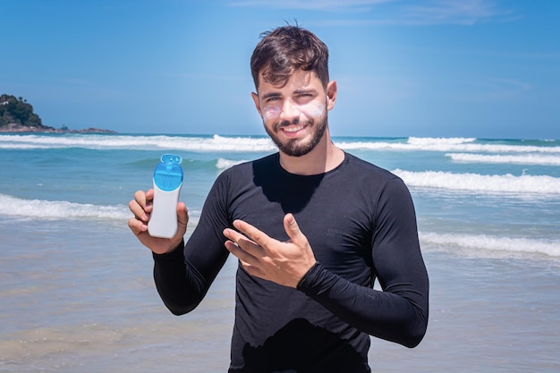 Bell'uomo sulla spiaggia che applica la crema solare per proteggersi dal sole.