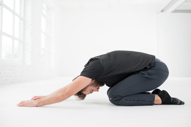 Photo handsome man in the black sportswear doing yoga in the white gym interior