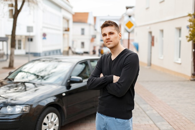 Handsome man in a black T-shirt near a car in the city