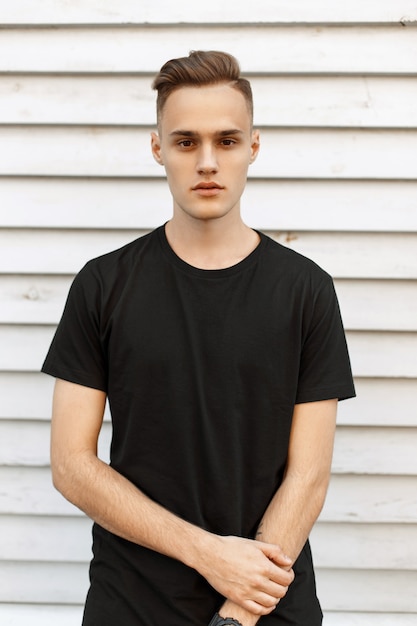 Handsome man in black t-shirt near the white wooden wall.