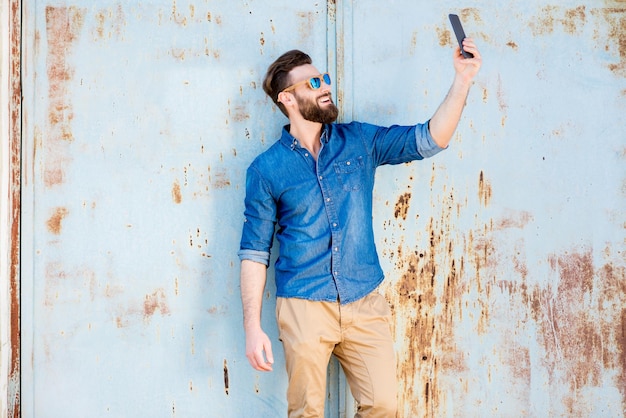 Handsome man in blue t-shirt with phone on the old rusty wall background