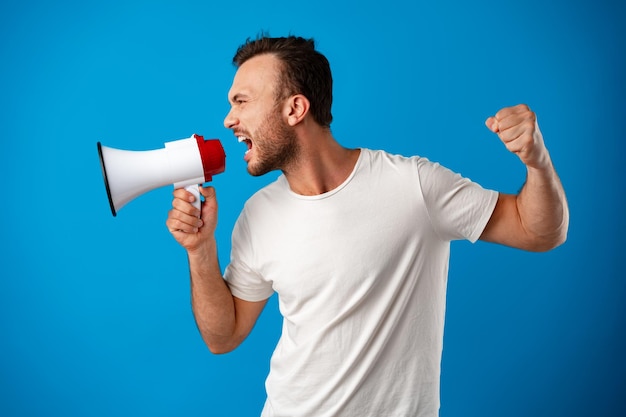 Handsome man over blue wall shouting through a megaphone