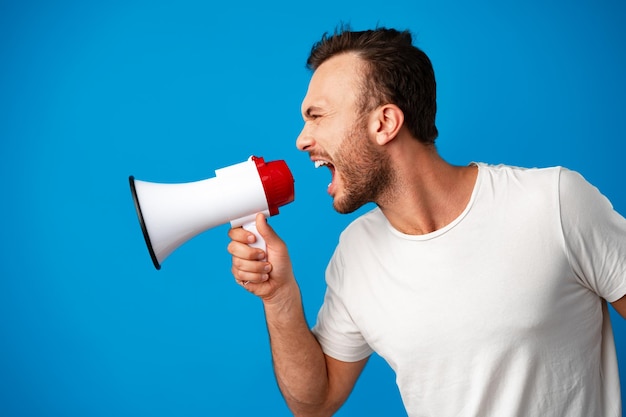 Handsome man over blue wall shouting through a megaphone