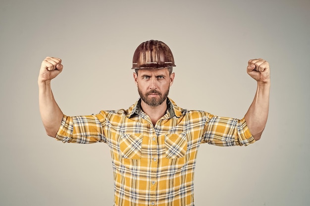 Фото Красивый мужчина-строитель в строительном защитном шлеме и клетчатой рубашке демонстрирует силу на строительной площадке