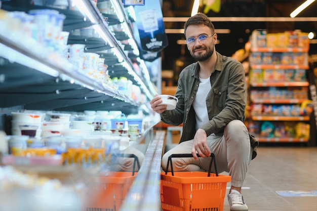 Красивый мужчина покупает здоровую еду и напитки в современном супермаркете или продуктовом магазине.