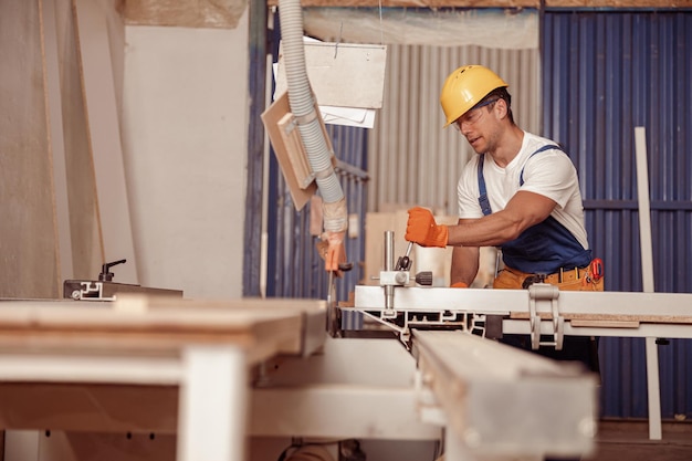 Handsome man carpenter using woodworking machine in workshop