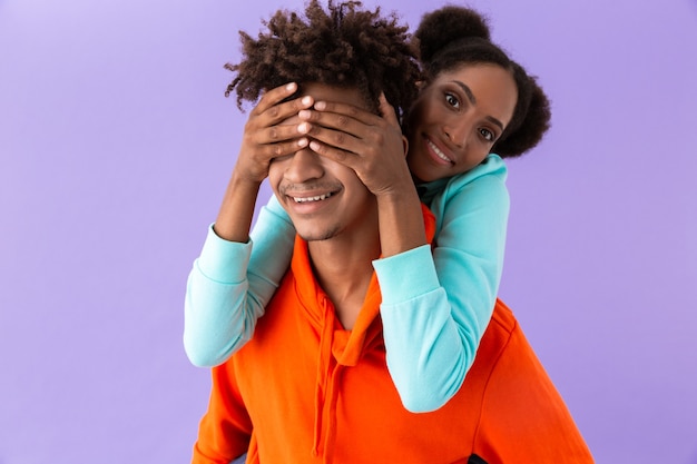 handsome man carrying young sister on his back, isolated over violet wall