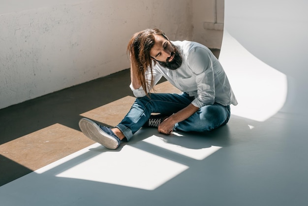 Foto bell'uomo in abbigliamento casual con i capelli lunghi seduto sul pavimento