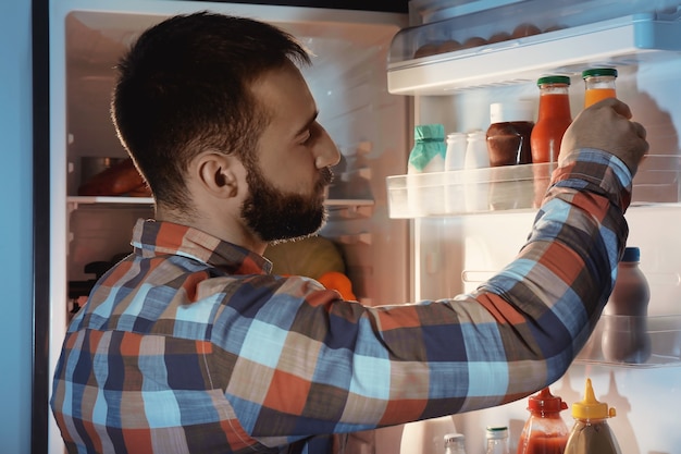 Handsome man choosing drink in refrigerator at night