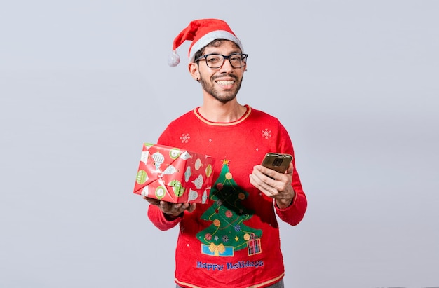 Handsome man in christmas hat holding gift and looking at phone\
guy in christmas hat holding gift box and smiling at smartphone\
christmas man holding gift box and telephone isolated