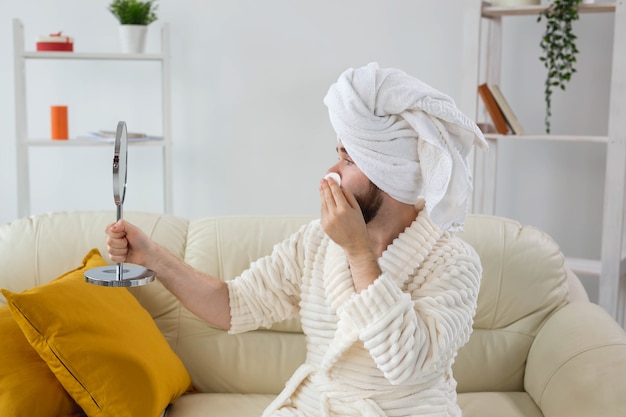 Handsome man cleaning face skin with batting cotton pads and\
looking at mirror. spa, body and skin care for male concept.