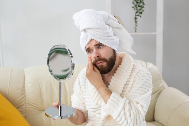 Handsome man cleaning face skin with batting cotton pads and\
looking at mirror spa body and skin