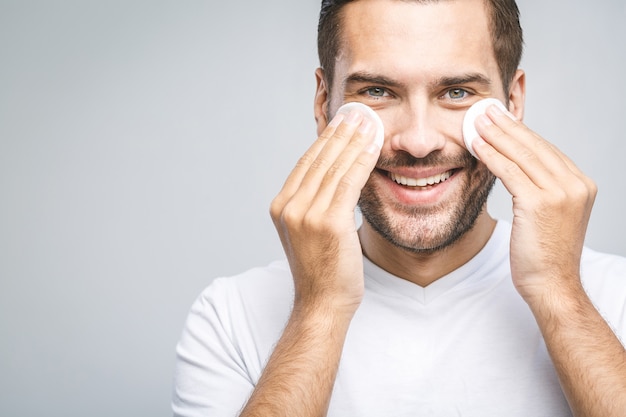 Uomo bello che pulisce la sua pelle con i dischetti di cotone