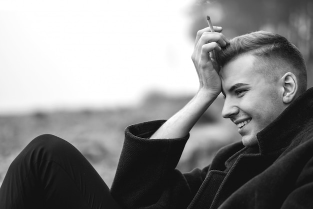 handsome man in a coat smokes a cigarette, art portrait of man, black and white photo