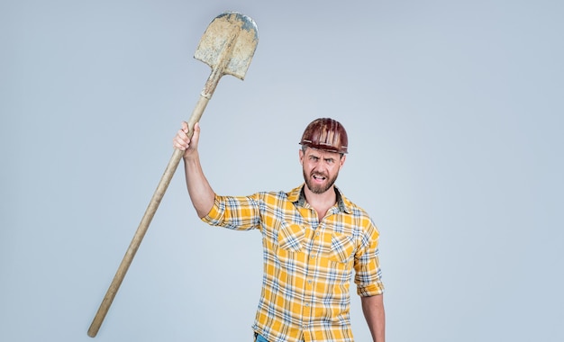 Handsome man contractor in construction safety helmet and checkered shirt on building site with shovel, labor day.