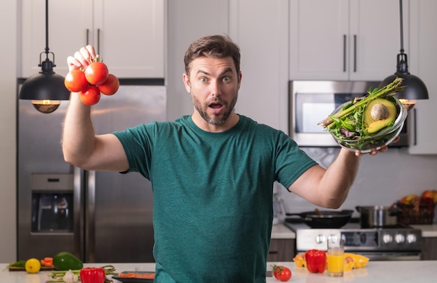 カジュアルな男の肖像画の野菜とキッチンに寄りかかってキッチン男でサラダを調理するハンサムな男