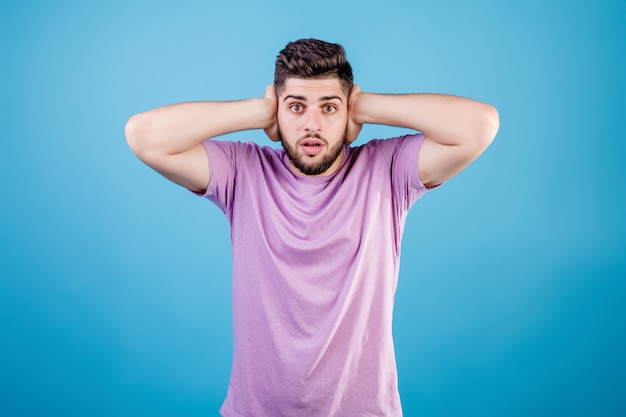 Handsome man covers ears with hands isolated on blue