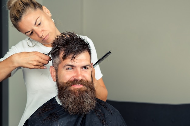 Bell'uomo taglia e rade barba e baffi. cliente hipster in visita al negozio di barbiere. acconciatura e taglio della barba.