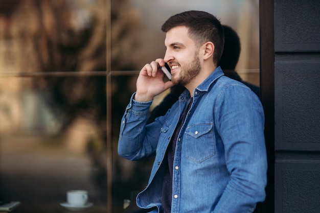 Красивый мужчина в джинсовой рубашке пользуется телефоном, стоя на улице