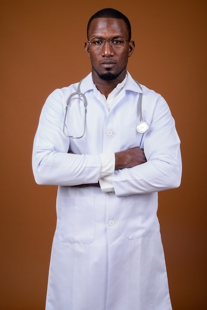 Handsome man doctor wearing eyeglasses against brown 