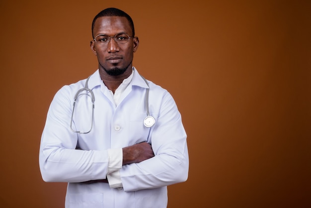 Handsome man doctor wearing eyeglasses against brown 