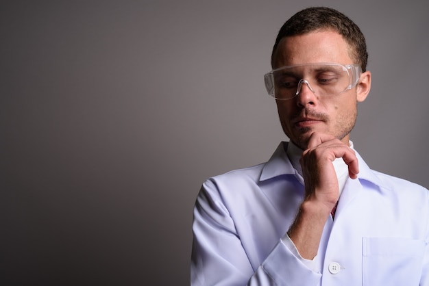 Handsome man doctor wearing protective glasses on gray back