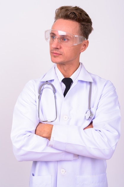 красивый мужчина-врач со светлыми вьющимися волосами в защитных очках у белой стены