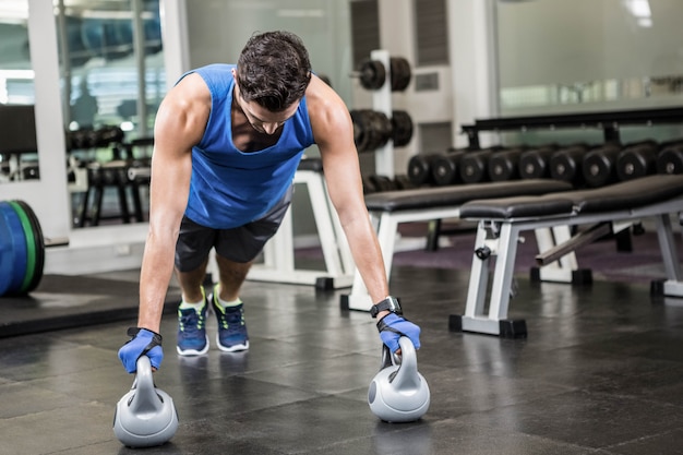 밀어 넣기를하는 잘 생긴 남자 체육관에서 kettlebells와 업