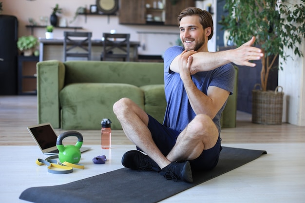 Handsome man doing stretching exercise at home during quarantine. Concept of healthy life.