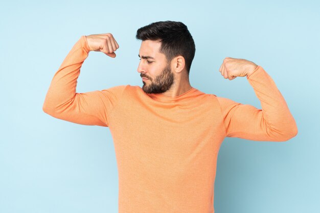 Handsome man doing strong gesture over isolated blue wall