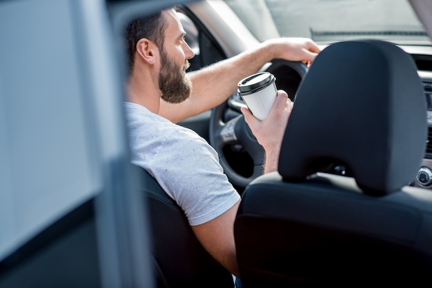 行くためにコーヒーで車を運転する白いTシャツを着たハンサムな男