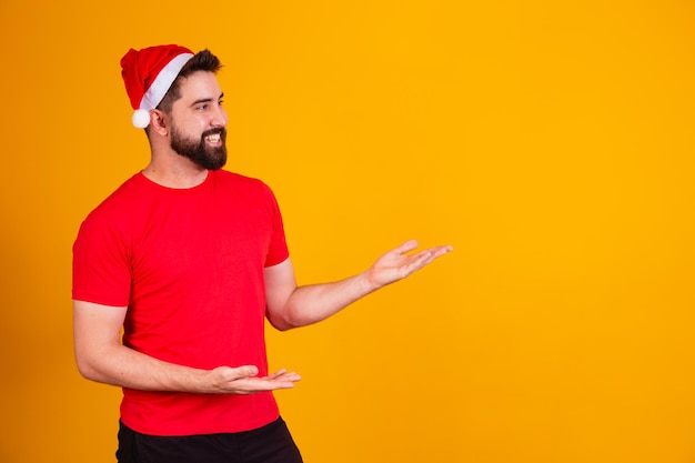 무료 텍스트 공간을 가리키는 산타 클로스 모자를 쓰고 크리스마스 옷을 입은 잘생긴 남자. 연말 프로모션